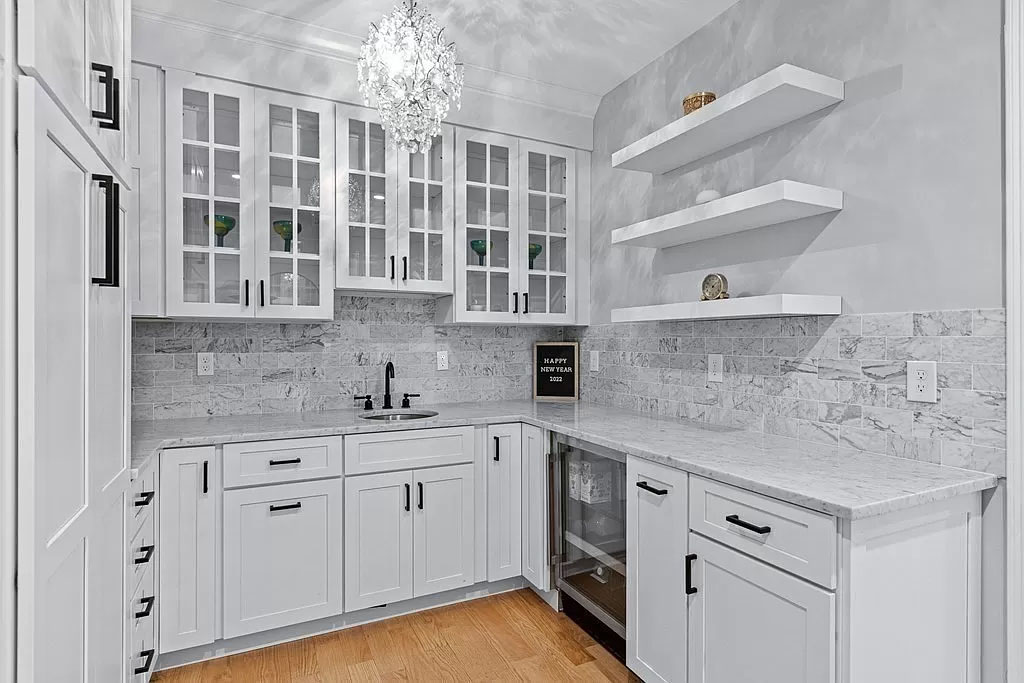 White shaker cabinets in pantry with floating shelves and wine fridge.