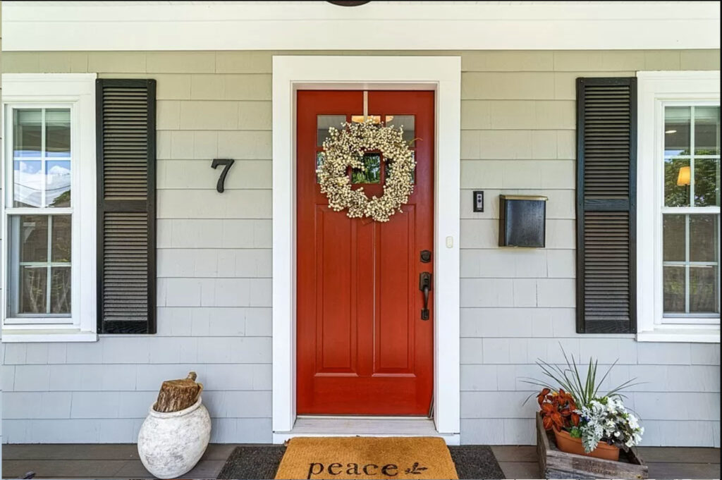 Front door of a home with sage green cedar shaker siding and a bright red door.